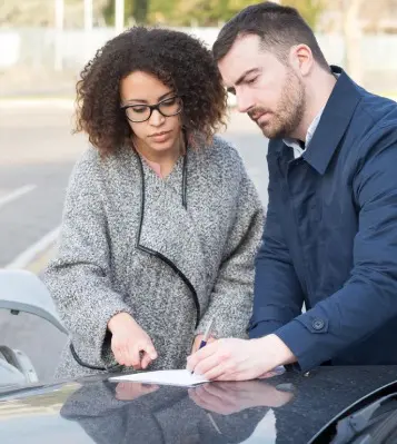 A man and woman signing papers on the hood of their car.